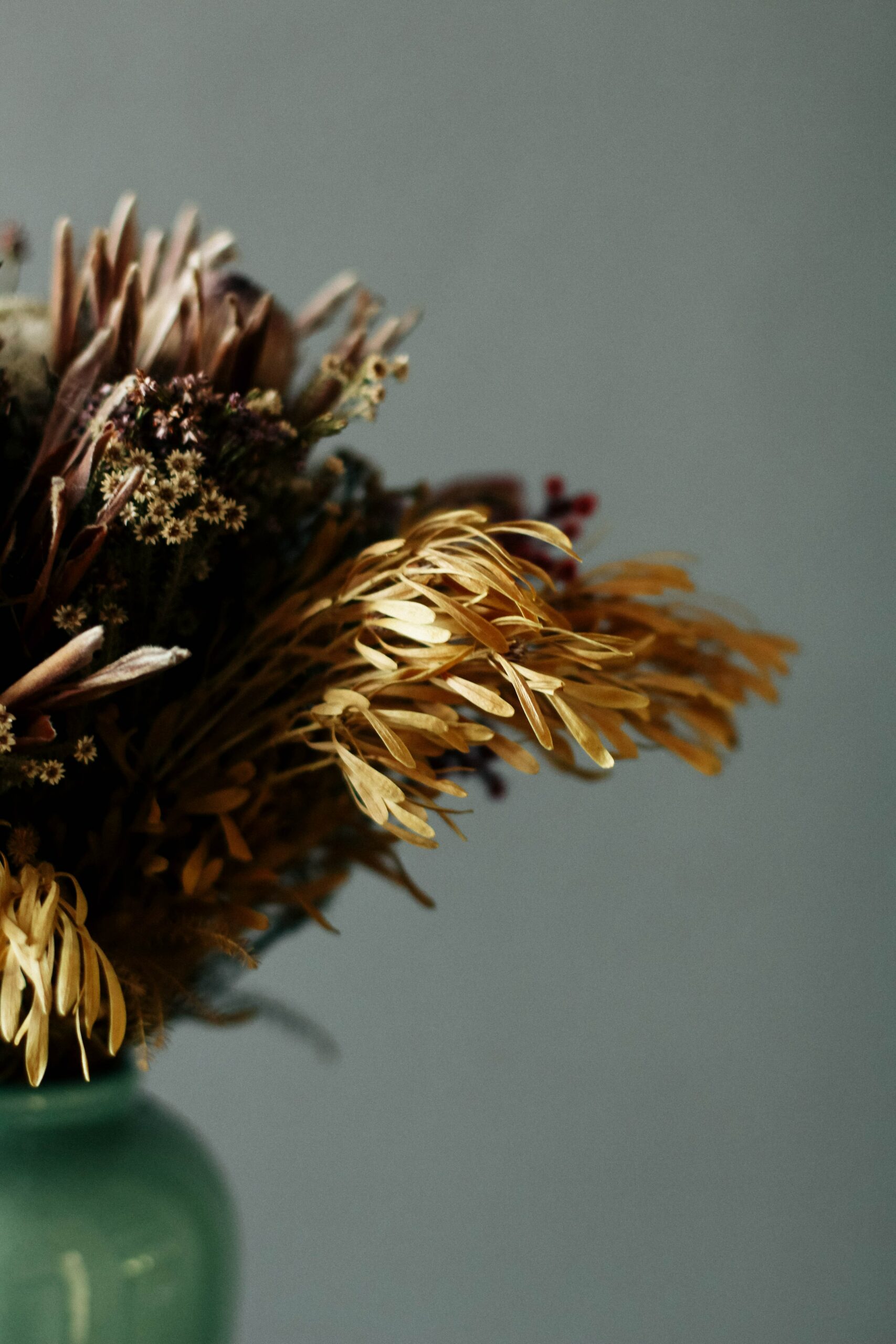 Trockenblumen in grüner Vase vor grauem Hintergrund