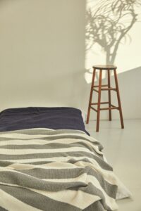 Schlichtes Schlafzimmer mit Bett, gestreifter Decke und Holzstuhl im warmen Sonnenlicht
